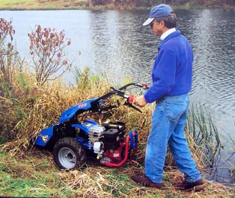 Man using BCS gardening equipment.  He is using the BCS tractor with sicklebar mower attachment for his lawn and garden needs. These BCS two wheel tractors have interchangeable attachemnts that make them a cultivator, brush mower, snowthrower, dozer, sicklebar mower, lawn mower, sweeper and chipper/shredder.